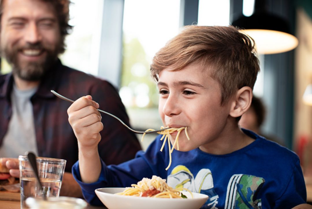 Junge isst Pasta in einer Raststaette